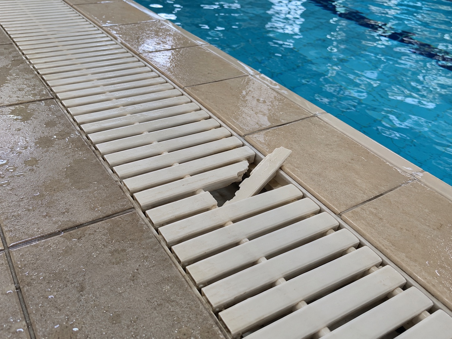 Illustrative generated photograph: cracked poolside drainage grate. Not a real incident photograph.
